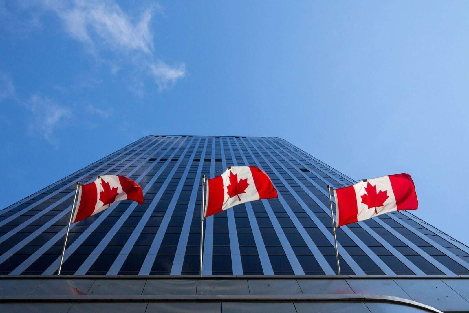 Picture of the canadian flag taken in front of a cold and blue business building in the CDB of Ottaawa. Ottawa is the capital city of Canada, and a major hub for economy, politics and business in America.